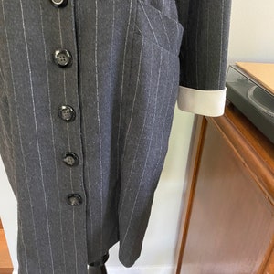May include: A grey pinstripe dress with a white collar and white cuffs. The dress has a button-up front and a pocket on the left side.