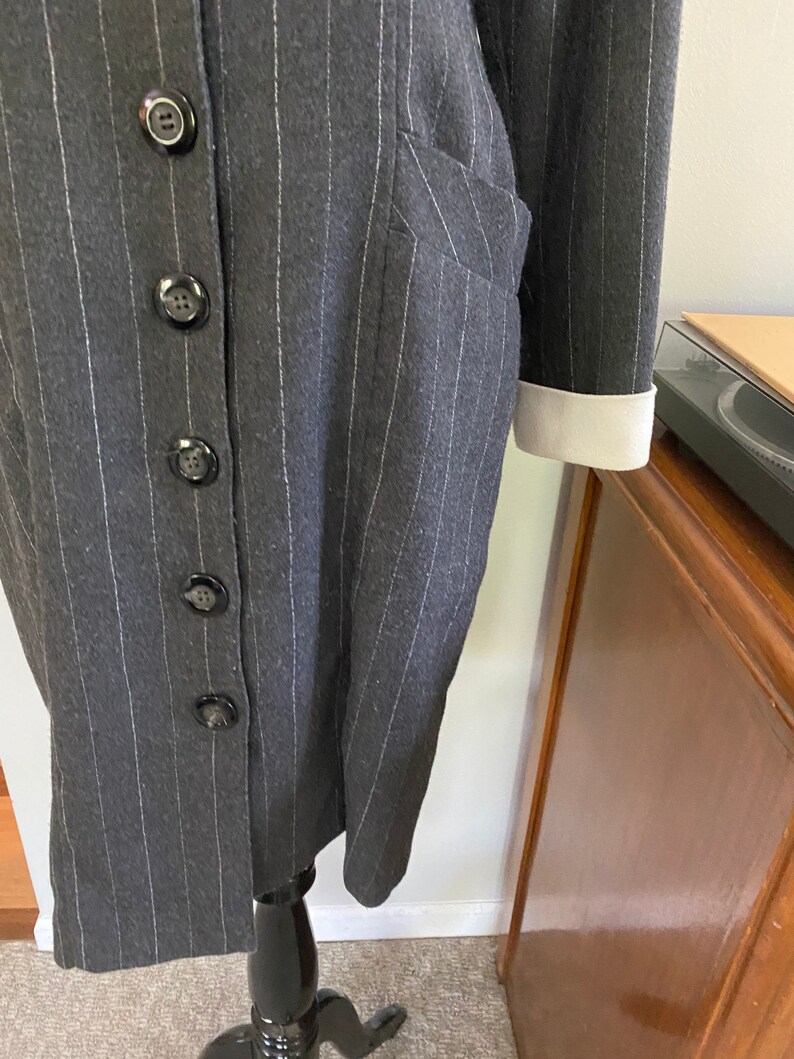 May include: A grey pinstripe dress with a white collar and white cuffs. The dress has a button-up front and a pocket on the left side.