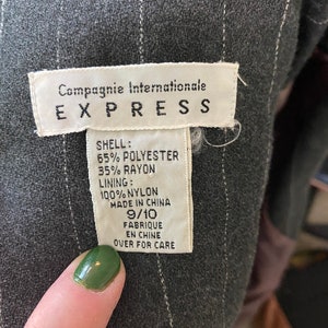 May include: A white tag with black text that reads "Compagnie Internationale EXPRESS" and details the fabric composition of the garment. The tag says "SHELL: 65% POLYESTER 35% RAYON LINING: 100% NYLON MADE IN CHINA 9/10 FABRIQUE EN CHINE OVER FOR CARE".