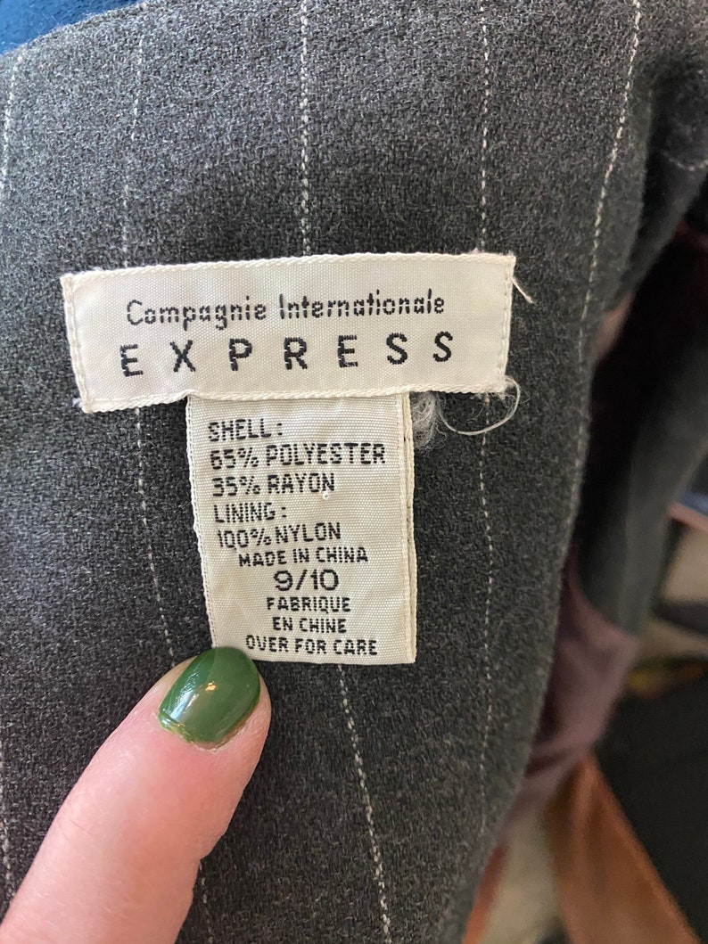 May include: A white tag with black text that reads "Compagnie Internationale EXPRESS" and details the fabric composition of the garment. The tag says "SHELL: 65% POLYESTER 35% RAYON LINING: 100% NYLON MADE IN CHINA 9/10 FABRIQUE EN CHINE OVER FOR CARE".