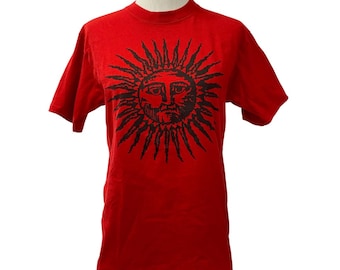 May include: Red short-sleeved t-shirt with a black sun graphic featuring a face.