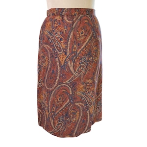 May include: A knee-length skirt featuring a paisley design in rust, blue, and gold hues. The skirt has a fitted waist and a straight cut. The fabric appears to be woven.