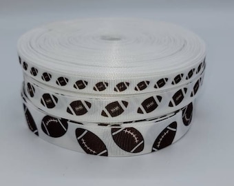 May include: White ribbon with a brown football pattern. The ribbon is rolled up and ready to be used for crafts or decorations.