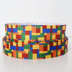 May include: Two rolls of colorful ribbon with a pattern of colorful blocks, resembling building blocks. The ribbon is yellow, red, blue, and green.