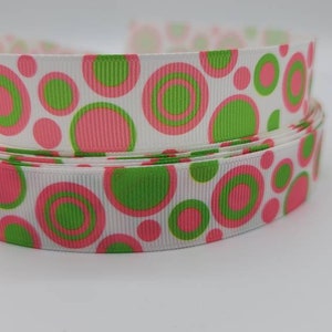 May include: White ribbon with a pink and green polka dot pattern. The ribbon is folded in half and the polka dots are of varying sizes.
