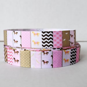 Puede incluir: Dos rollos de cinta estampada rosa, marrón y blanca con un diseño de caballo. La cinta es perfecta para manualidades y decoración.