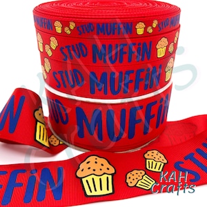 May include: Red ribbon with the words "STUD MUFFIN" in blue and cartoon muffins. The ribbon is rolled up in a spool, with a length of ribbon unrolled in the foreground. The ribbon is from KAH Crafts.