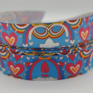 May include: A blue ribbon with a colorful rainbow and heart pattern. The ribbon is folded in a circle.