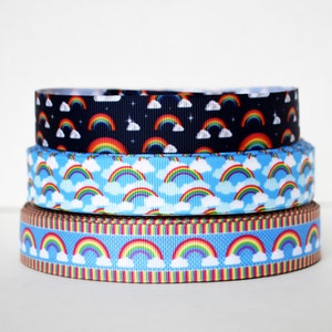 May include: Three rolls of rainbow ribbon with a blue background and white clouds. The top ribbon is black with white stars. The bottom ribbon has a brown and yellow stripe.