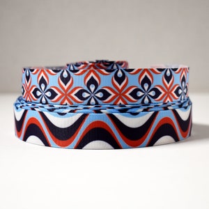 May include: Two rolls of patterned ribbon. The top roll has a blue background with red and white geometric flowers. The bottom roll has a white background with red, blue, and black wavy lines.