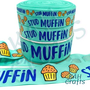 May include: A roll of teal ribbon with the words "STUD MUFFIN" in blue, and a cartoon muffin graphic. The ribbon is suitable for crafting, gift wrapping, or adding a decorative touch to various projects.