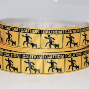 Puede incluir: Cinta amarilla con señales de precaución negras que dicen "CAUTION" y representan a una persona corriendo lejos de un perro. La cinta está enrollada.