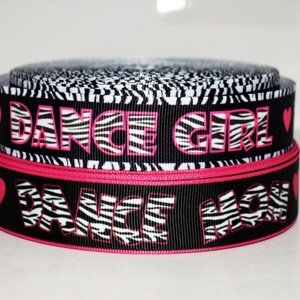 May include: Two spools of ribbon. The top spool has a black and white zebra print with the words "DANCE GIRL" in pink. The bottom spool has the words "DANCE MOM" in white zebra print with a pink border and pink hearts.