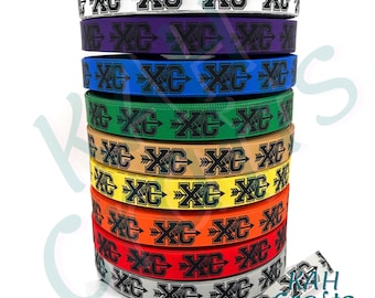 May include: A stack of 10 different colored ribbon spools with a black and white design of an arrow and the letters "XC".
