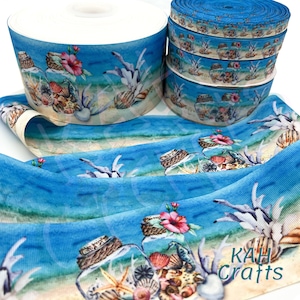 May include: A blue and white ribbon with a watercolor design of seashells, starfish, and coral in glass jars. The ribbon is folded and shows the design repeating. The ribbon is labeled "KAH Crafts".