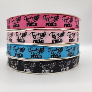 May include: Four rolls of ribbon with the words "Track & Field" and a running shoe with wings printed on them. The ribbon colors are pink, light pink, blue, and black.