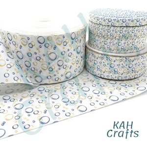 May include: White ribbon rolls with a repeating pattern of blue and gold bubbles. The ribbon is displayed in various sizes, with the largest roll unspooled to show the pattern. The text "KAH Crafts" is in the bottom right corner.