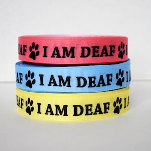 May include: Three rolls of ribbon in pink, blue, and yellow with black paw prints and the text "I AM DEAF" printed on each.