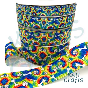 May include: A roll of colorful tie-dye ribbon with white paw prints and bone designs. The ribbon is in shades of blue, green, yellow, and red.
