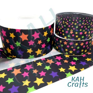 May include: Black ribbon with a colorful star pattern. The stars are in shades of pink, yellow, green, and purple. The ribbon is rolled up and ready to be used for crafts or decorations.