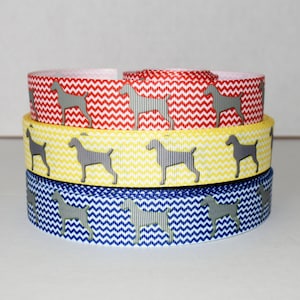 May include: Three rolls of chevron patterned ribbon with a grey silhouette of a dog on each roll. The ribbon colors are red, yellow, and blue.