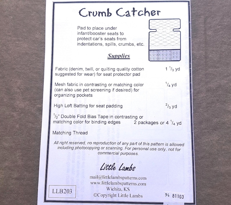Pu&ograve; includere: Un foglio di carta bianco con il titolo "Crumb Catcher" e un diagramma di un proteggi-sedile per auto. Il testo elenca i materiali necessari, tra cui tessuto, tessuto a rete, ovatta e sbieco. Il modello &egrave; di Little Lambs.