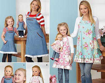 May include: Simplicity pattern 1240 featuring aprons for adults and children, with matching aprons for dolls. The aprons are in denim, floral, and polka dot designs. The image shows a variety of apron styles with ruffle and pocket details.