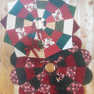 May include: Two quilted tree skirts with a floral design. The top skirt is a star shape with red, green, and cream-colored fabric. The bottom skirt is a flower shape with red and black fabric. Both have a center opening and a bow.