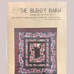 May include: A brochure for "The Buggy Barn," a quilt shop, featuring a quilt with pink and green floral patterns. The shop's name and address are printed at the top, along with the hours of operation.