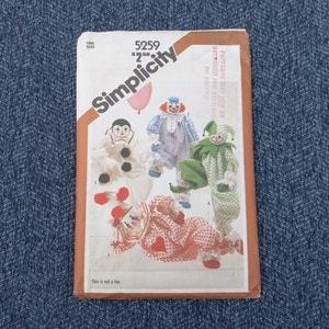 May include: A vintage Simplicity sewing pattern featuring illustrations of clown dolls. The pattern cover displays several clown designs in various colors, including red, white, blue, and green. The text "This is not a toy" is visible at the bottom.