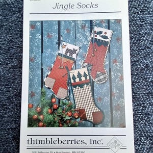 May include: A pattern for "Jingle Socks" featuring three Christmas stockings with various patterns and embellishments. The stockings are red, white, and green, with a rustic, homespun aesthetic. The pattern is from thimbleberries, inc.