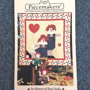 May include: A printed paper featuring a quilt design with rag doll figures and a heart-shaped balloon. The quilt has a red, white, and blue color scheme. The text "Piecemakers" and "In Honor of Rag Dolls" are visible.