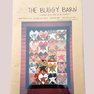 May include: A quilt pattern featuring a patchwork design of stars and hearts in various fabrics. The quilt is displayed on a wooden background. The text "THE BUGGY BARN" and shop details are visible at the top.