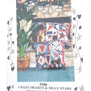 May include: A brochure for DuAnn's Designs features two floor pillows with patchwork designs. The pillows are approximately 28 inches square and have a Crazy Hearts & Silly Stars theme. The background includes a fireplace and a potted plant.