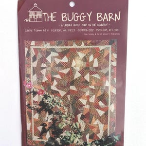 May include: A brochure for "The Buggy Barn," a quilt shop, featuring a colorful quilt design. The brochure's burgundy background displays the shop's name, address, and hours. The quilt pattern includes triangles and various fabric patterns.