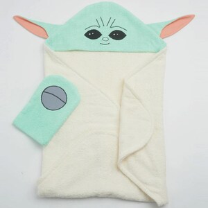 May include: A hooded baby towel and washcloth set. The towel is cream-colored with a light green hood featuring a character's face with large eyes and ears. The washcloth is light green with a gray circle design.