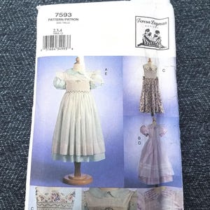 May include: A sewing pattern by Teresa Layman Designs, featuring illustrations of children's dresses. The pattern number is 7593, with sizes 2, 3, and 4. The dresses have various styles, including puff sleeves and floral details.
