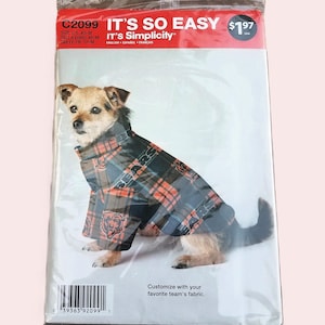 May include: A dog wearing a plaid jacket is inside a Simplicity pattern package. The pattern is for a dog coat and includes the text "IT'S SO EASY" and "Customize with your favorite team's fabric."