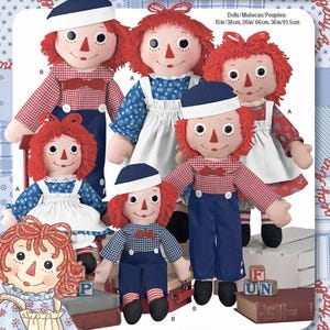 May include: A collection of Raggedy Ann dolls in various sizes. The dolls have red yarn hair, painted faces, and wear outfits in blue, red, and white. Some dolls wear sailor hats. The image includes text that reads "Dolls/Muñecas/Poupées: 15in/38cm, 26in/66cm, 36in/91.5cm".