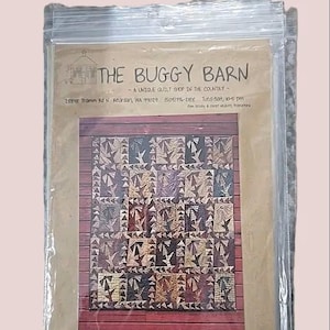 May include: A packaged quilt pattern from "The Buggy Barn." The pattern features a quilt design with geometric shapes in shades of brown, tan, and purple. The packaging includes the shop's name, address, and hours.