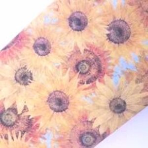 May include: A patterned fabric or paper featuring a repeating watercolour-style illustration of sunflowers with yellow petals and dark brown centres. The floral design is set against a light blue background, creating a bright and botanical aesthetic.