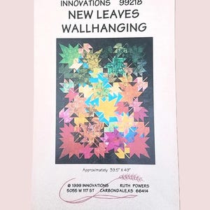 May include: A printed paper with the text "INNOVATIONS NEW LEAVES WALLHANGING". The image on the paper is a colorful leaf pattern. The dimensions are approximately 100cm x 124cm.