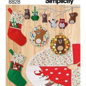 May include: Simplicity 8828 sewing pattern featuring felt Christmas stockings, ornaments, and a tree skirt. The designs include a bear, owl, moose, snowman, and fox. The items are decorated with colourful polka dots, white pom-pom trim, and snowflake motifs.