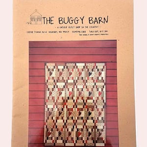 May include: A quilt pattern displayed on a red wooden wall. The quilt features a patchwork design with various patterns in shades of brown, red, and cream. The top of the image shows a brown paper with the text "THE BUGGY BARN".