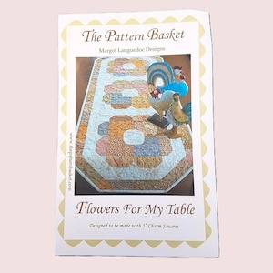 May include: A brochure for "Flowers For My Table" by The Pattern Basket. The brochure features a colorful floral table runner design made with 12.7 cm charm squares. The brochure also features a rooster figurine.