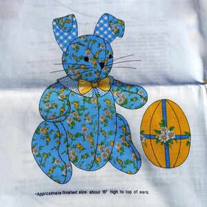 May include: A blue fabric bunny with a floral pattern and a yellow bow tie, next to a yellow Easter egg with blue stripes and floral accents. The bunny is approximately 16 inches tall.