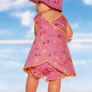 May include: A baby wearing a pink floral print sun hat and matching wrap-style dress with yellow trim. The outfit includes matching bloomers. The baby is standing outside with a blue sky background.