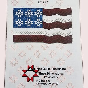 May include: A printed pattern for a 3-D patchwork quilt, titled "Long May She Wave." The quilt design resembles the American flag, measuring 42" x 27". The pattern is published by "nimas Quilts Publishing" in Durango, CO.