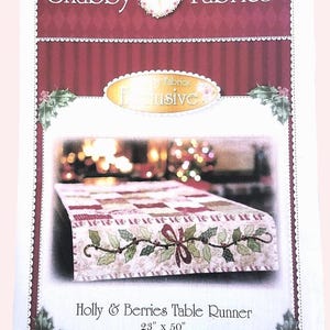 May include: A product image for a Holly & Berries table runner. The runner is 23 inches by 50 inches, featuring a festive design with holly leaves, berries, and a bow. The background is a blurred image of a decorated Christmas tree.