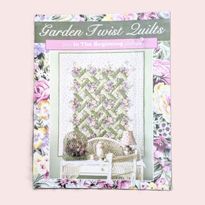 May include: A book cover titled "Garden Twist Quilts" with a floral design. The cover features a quilt with a green and floral pattern, a white wicker chair, and a birdcage. The border is decorated with pink and purple flowers.